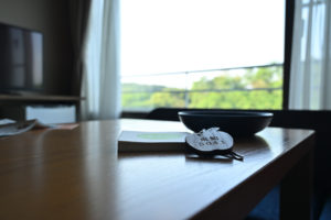 青森・星野リゾート青森屋、自然光が差し込む窓辺に置かれた、りんご型の木製キーホルダーが付いたルームキーの温もりある情景（撮影:Nikon Z6III）